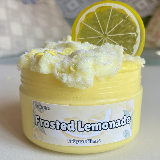 A jar is filled with yellow butter slime with a sparkly light yellow cloud slime on top. It's further topped with clay fimo lemons and a plastic lemon charm. The label reads "Frosted Lemonade, Babycat Slimes"