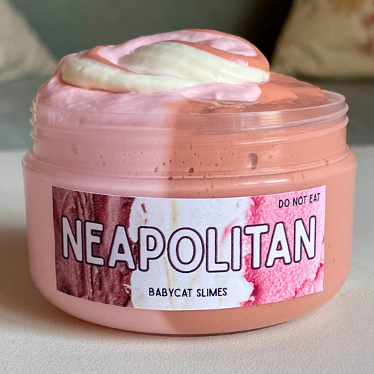 A jar is filled with pink, white, and brown butter slime resembling Neapolitan ice cream. The label reads Neapolitan Babycat Slimes.