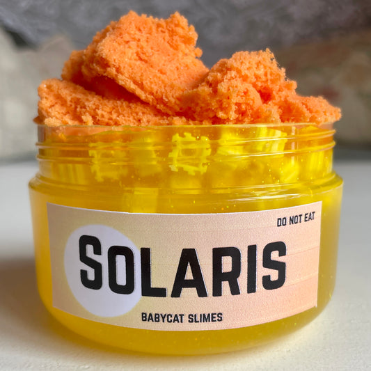 A jar is filled with sparkling yellow clear slime with yellow block beads, and topped with fluffy orange cloud slime. The label reads "Solaris - Babycat Slimes"