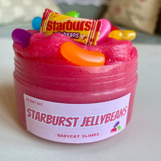A jar is filled with dark pink jelly slime and jellybean and candy bag charms on top. Label says Starburst Jellybeans Babycat Slimes.
