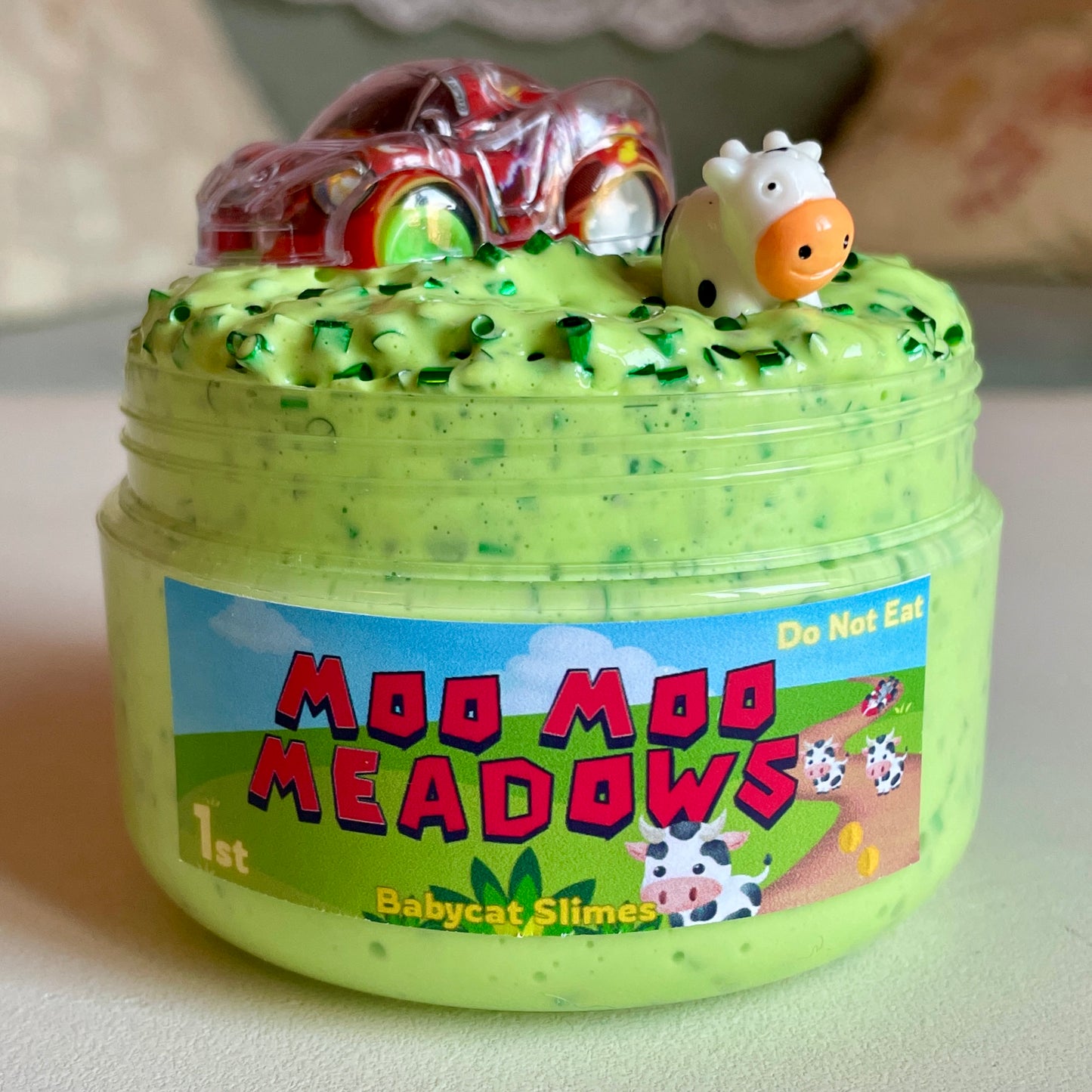 Green crunchy slime in a container with 'Moo Moo Meadows' label and toy cow on top.